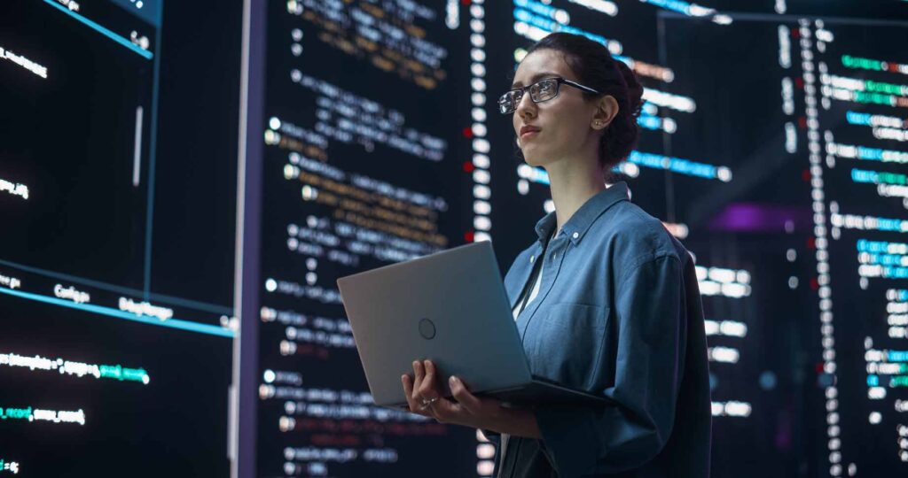 Mujer con un portátil frente a pantallas con datos, en uno de los trabajos con más futuro para 2030