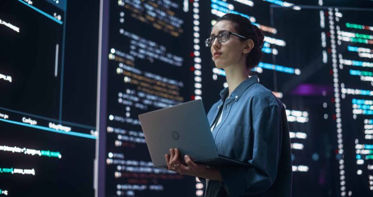 Mujer con un portátil frente a pantallas con datos, en uno de los trabajos con más futuro para 2030
